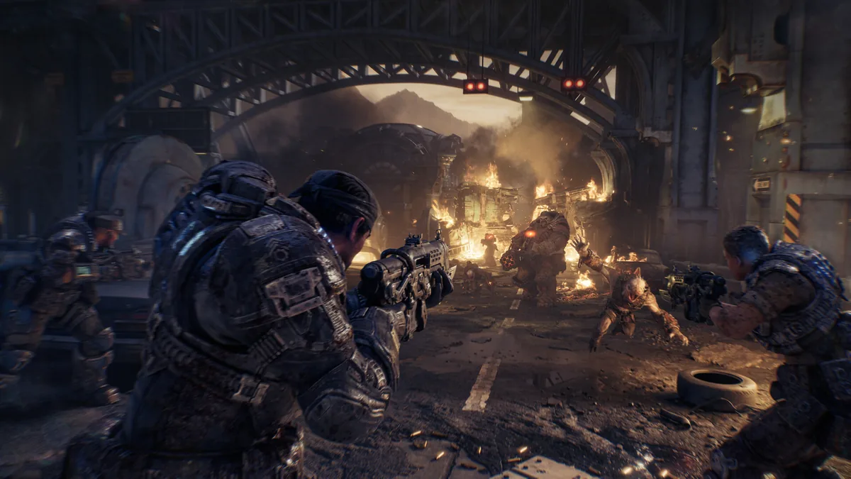 لقطة من أسلوب اللعب في Gears of War: E-Day حيث يقتحم أعداء شارعًا محترقًا تحت جسر صناعي